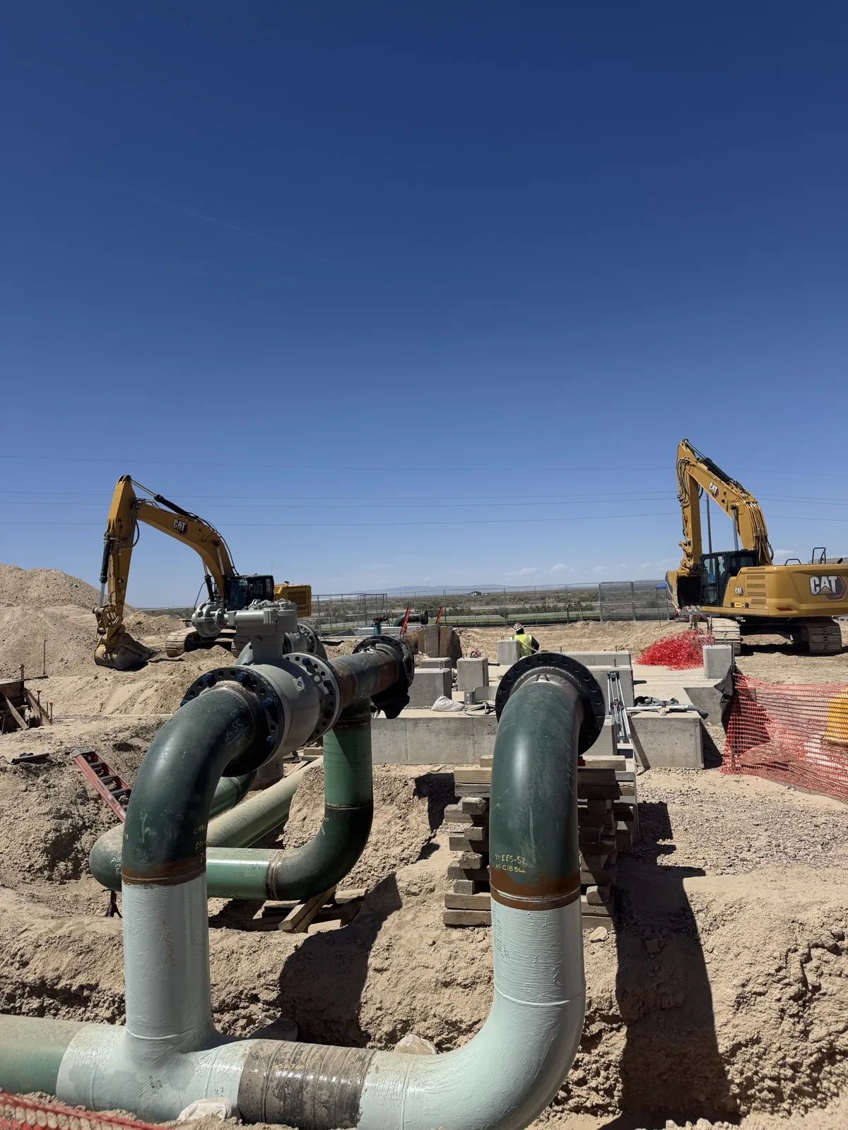 Wide view of natural gas pipe assembly under installation with CAT excavators on either side